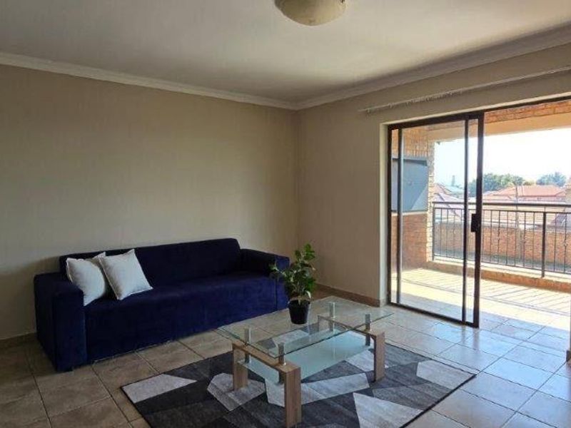 A living room featuring tiled flooring and a sliding glass door that opens onto a balcony, providing natural light and outdoor access.
