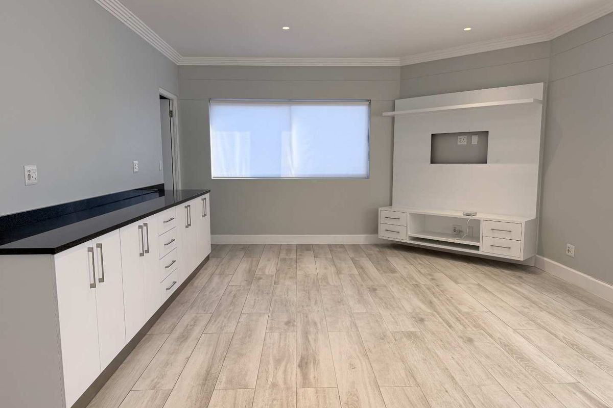 A bright, modern living room featuring light wood-look laminate flooring, built-in white cabinetry with dark stone countertops, and a custom media unit.