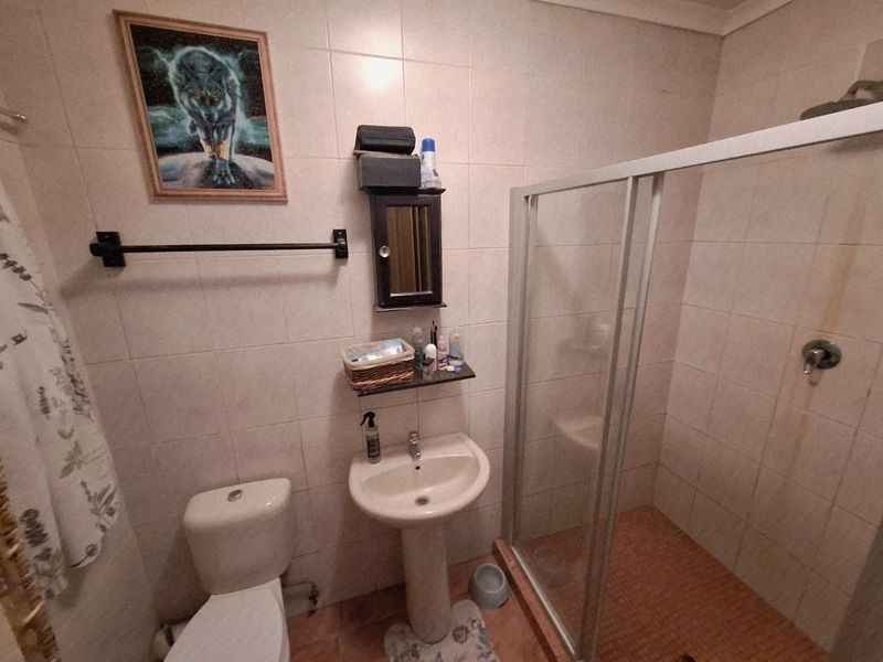 A functional bathroom featuring a pedestal sink, toilet, and a glass-enclosed shower with tiled finishes throughout.