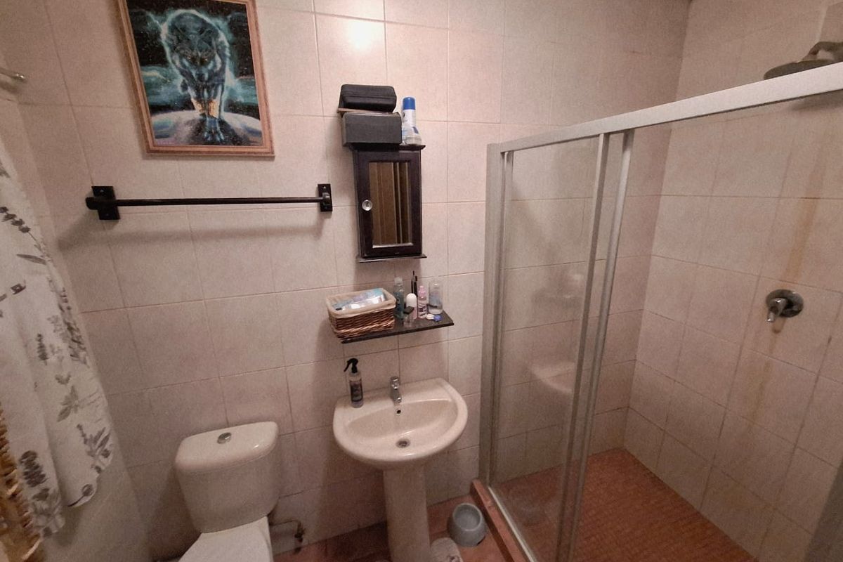 A functional bathroom featuring a pedestal sink, toilet, and a glass-enclosed shower with tiled finishes throughout.