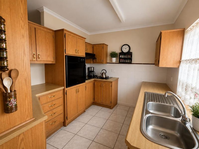 A functional kitchen featuring timber-look cabinetry, laminate countertops, a double stainless steel sink, and built-in cooking appliances with tiled splashbacks.