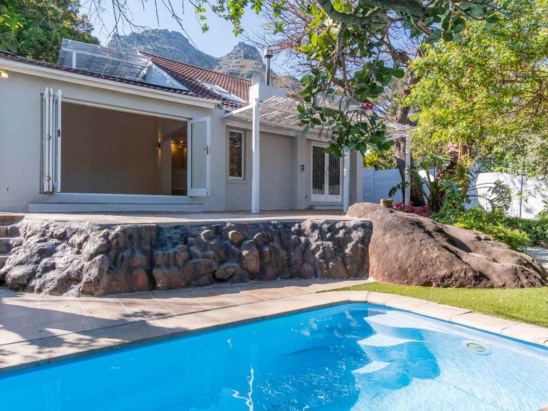 Rear exterior view featuring a swimming pool, stone retaining wall, tiled patio area, and bi-fold doors leading into the home.