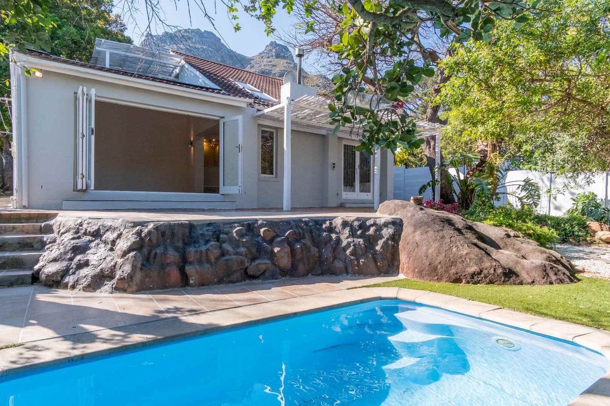 Rear exterior view featuring a swimming pool, stone retaining wall, tiled patio area, and bi-fold doors leading into the home.