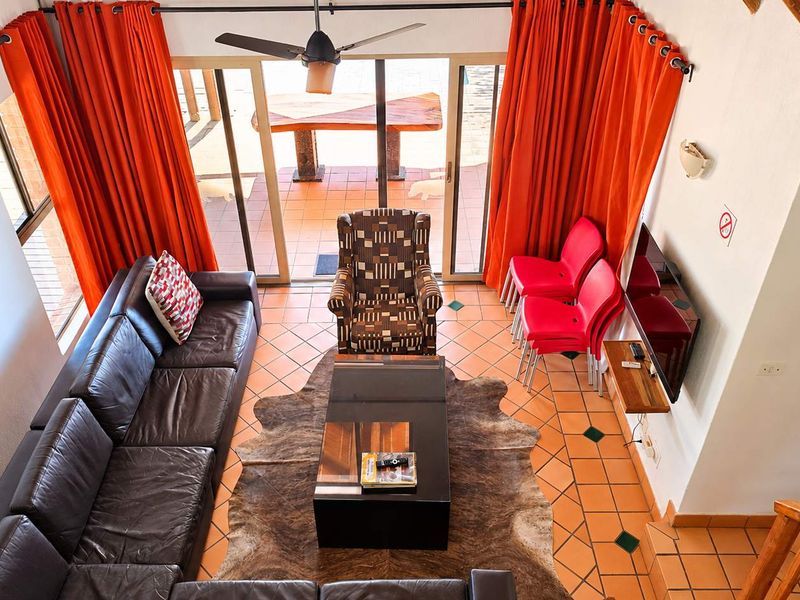 A living room featuring terracotta floor tiles, a ceiling fan, and large sliding glass doors that provide access to an outdoor patio area.