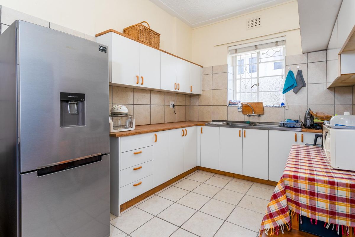 A functional kitchen featuring white cabinetry, wood-look countertops, tiled splashbacks, and a stainless steel sink with a window view.