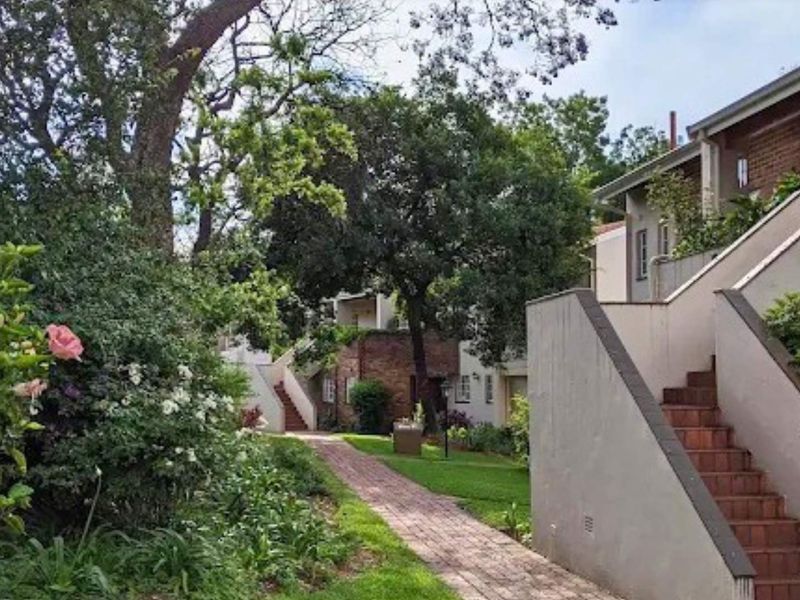 A view of the apartment complex exterior featuring a brick pathway, landscaped garden areas, and external staircases leading to the units.