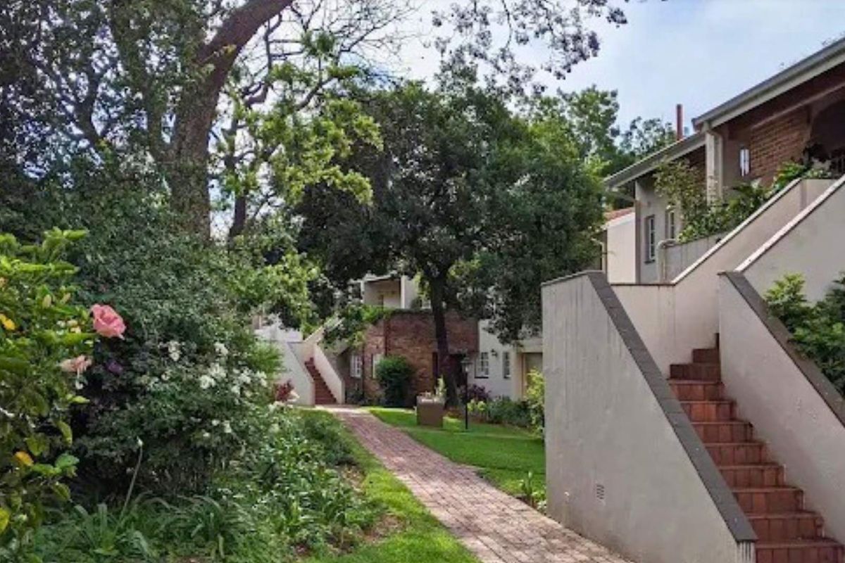 A view of the apartment complex exterior featuring a brick pathway, landscaped garden areas, and external staircases leading to the units.