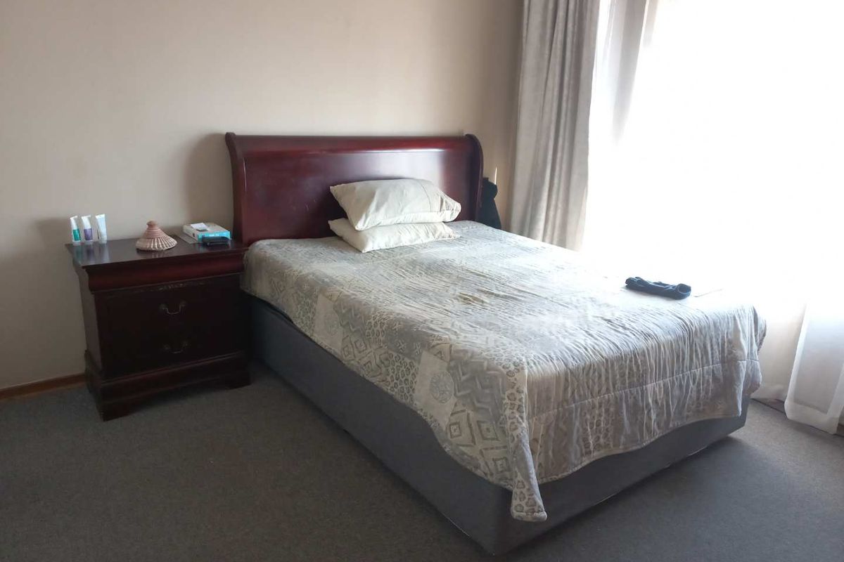 A standard bedroom featuring carpeted flooring and large windows with curtain tracks, providing natural light.