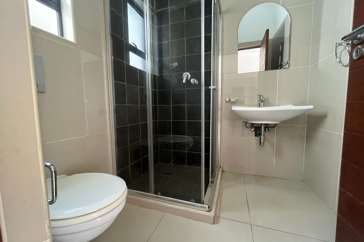 A compact bathroom featuring a glass-enclosed shower, wall-mounted basin, and toilet with neutral floor and wall tiling.