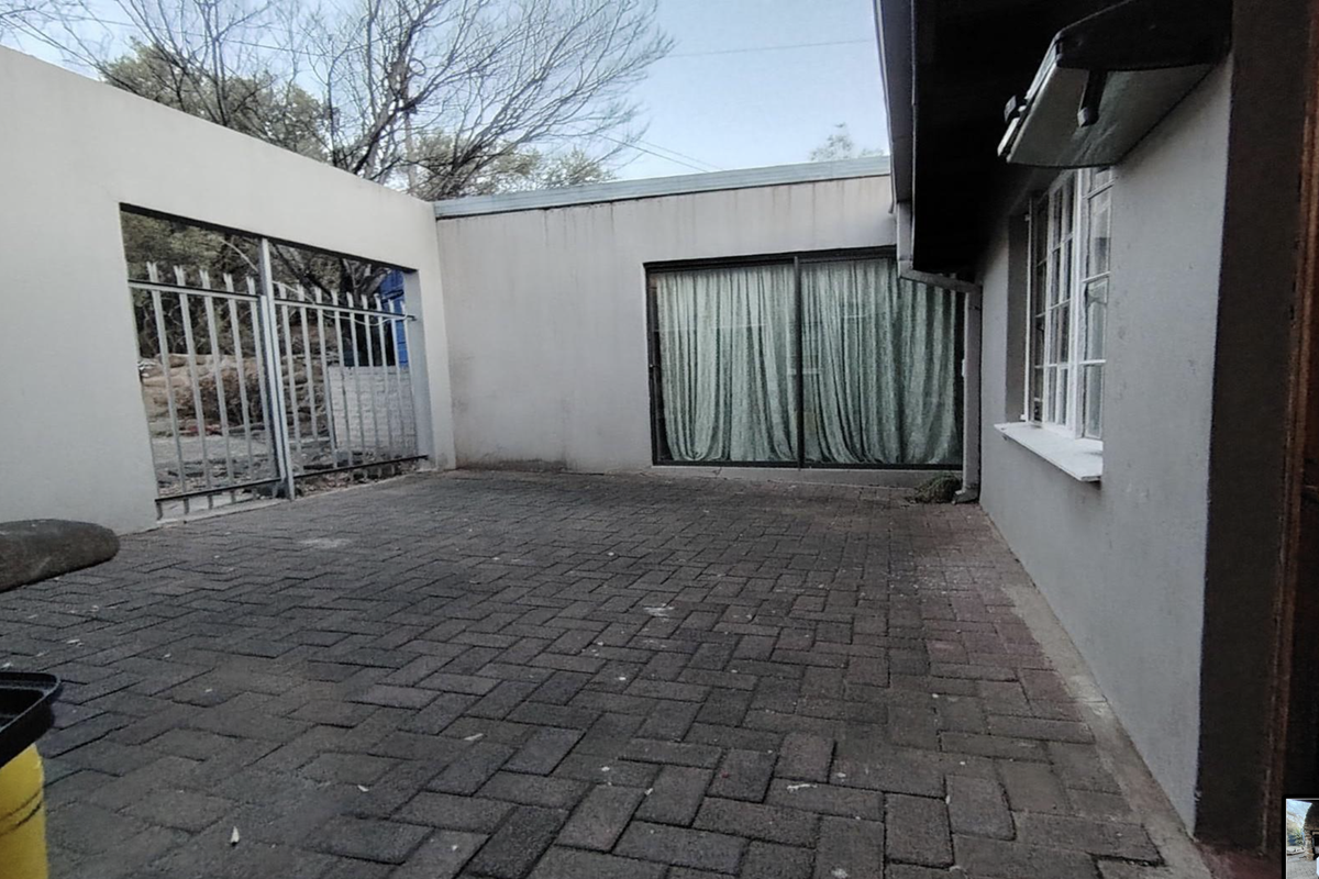 A paved rear courtyard area featuring a sliding glass door entrance and a secure metal gate, providing a private outdoor space.