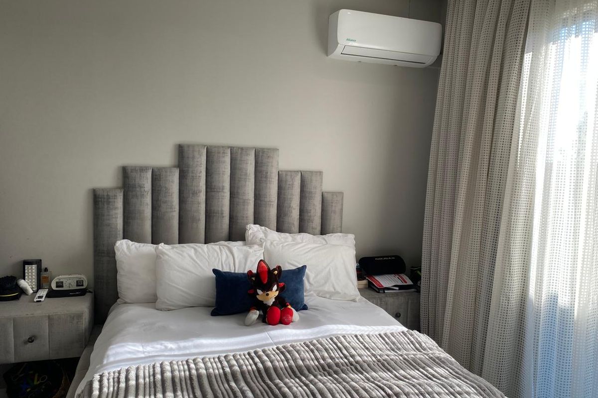 A well-maintained bedroom featuring a modern upholstered headboard, wall-mounted air conditioning unit, and floor-to-ceiling curtains.