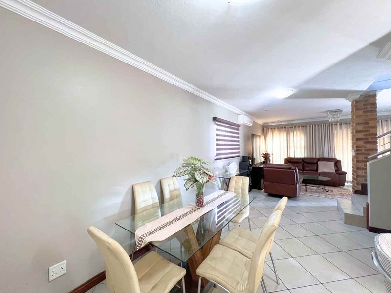 Open-plan living and dining area featuring ceramic floor tiles, crown molding, and an exposed brick feature pillar near the staircase.