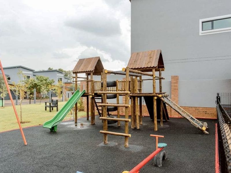 A communal outdoor play area featuring a wooden jungle gym, slide, and rubberized safety flooring located within the apartment complex grounds.
