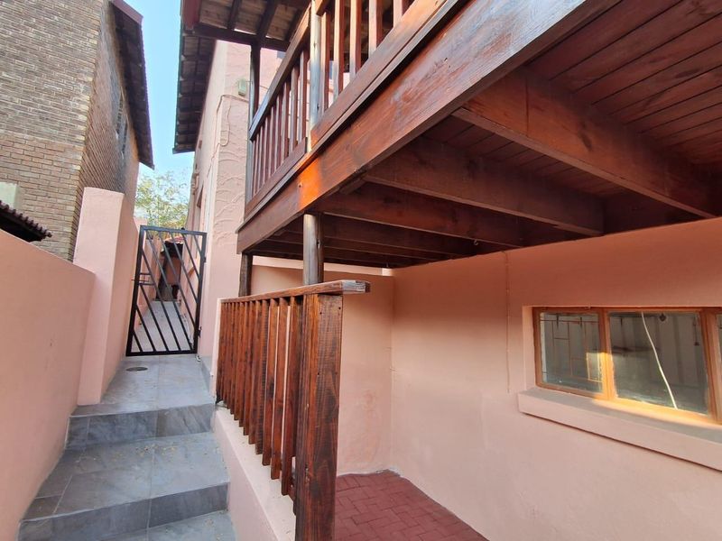Rear exterior view featuring a raised wooden balcony, security gate, and paved access path along the side of the property.