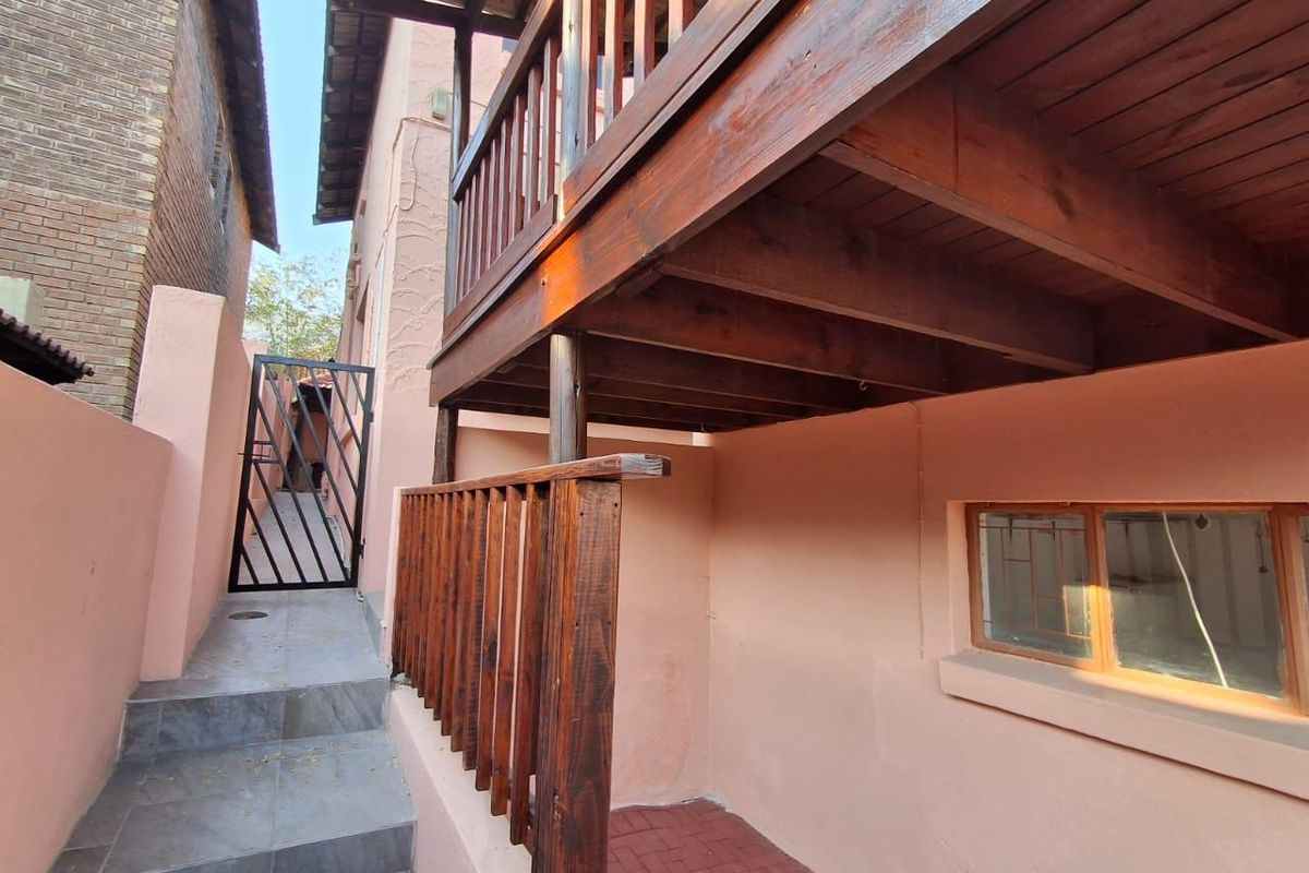 Rear exterior view featuring a raised wooden balcony, security gate, and paved access path along the side of the property.
