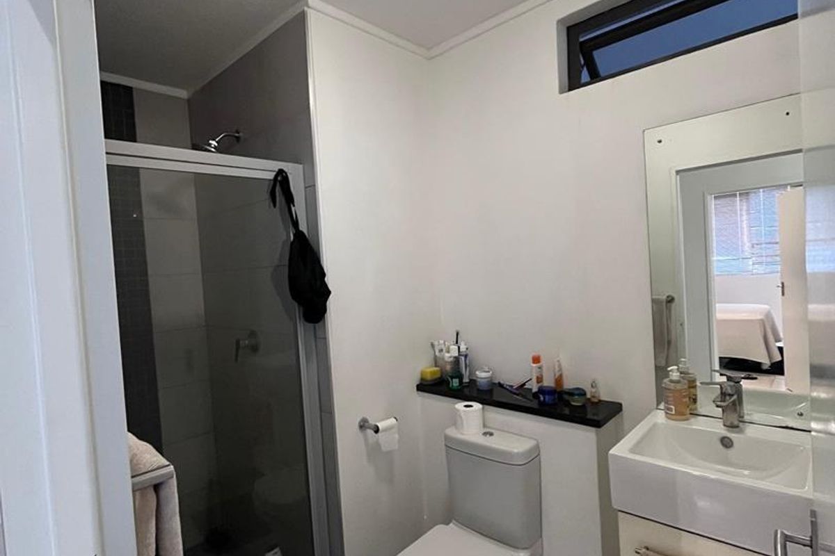 A compact bathroom featuring a glass-enclosed shower, a modern vanity with a basin, and a standard toilet with a built-in shelf.