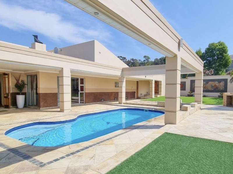 Spacious outdoor entertainment area featuring a swimming pool, covered patio, and a built-in brick braai, perfect for hosting and relaxation.