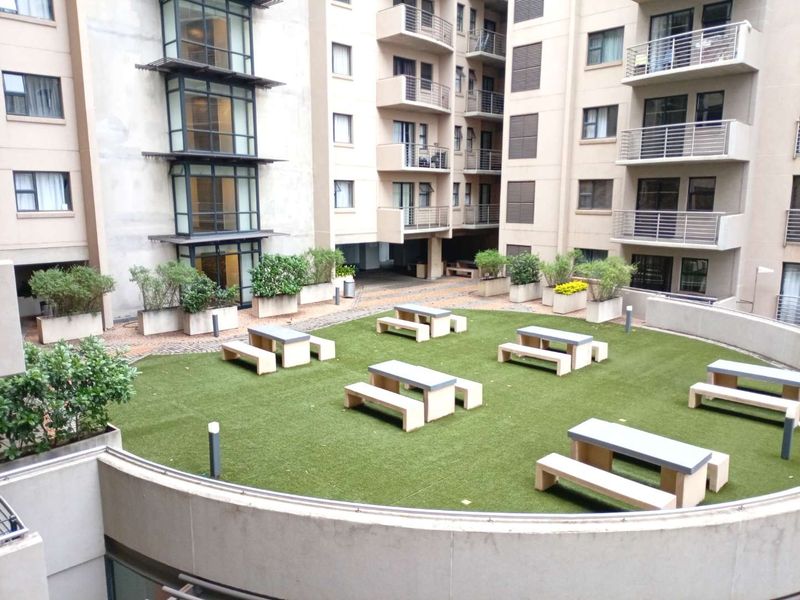 A communal courtyard area featuring artificial turf, fixed concrete seating, and landscaped planters, surrounded by the multi-story residential building structure.