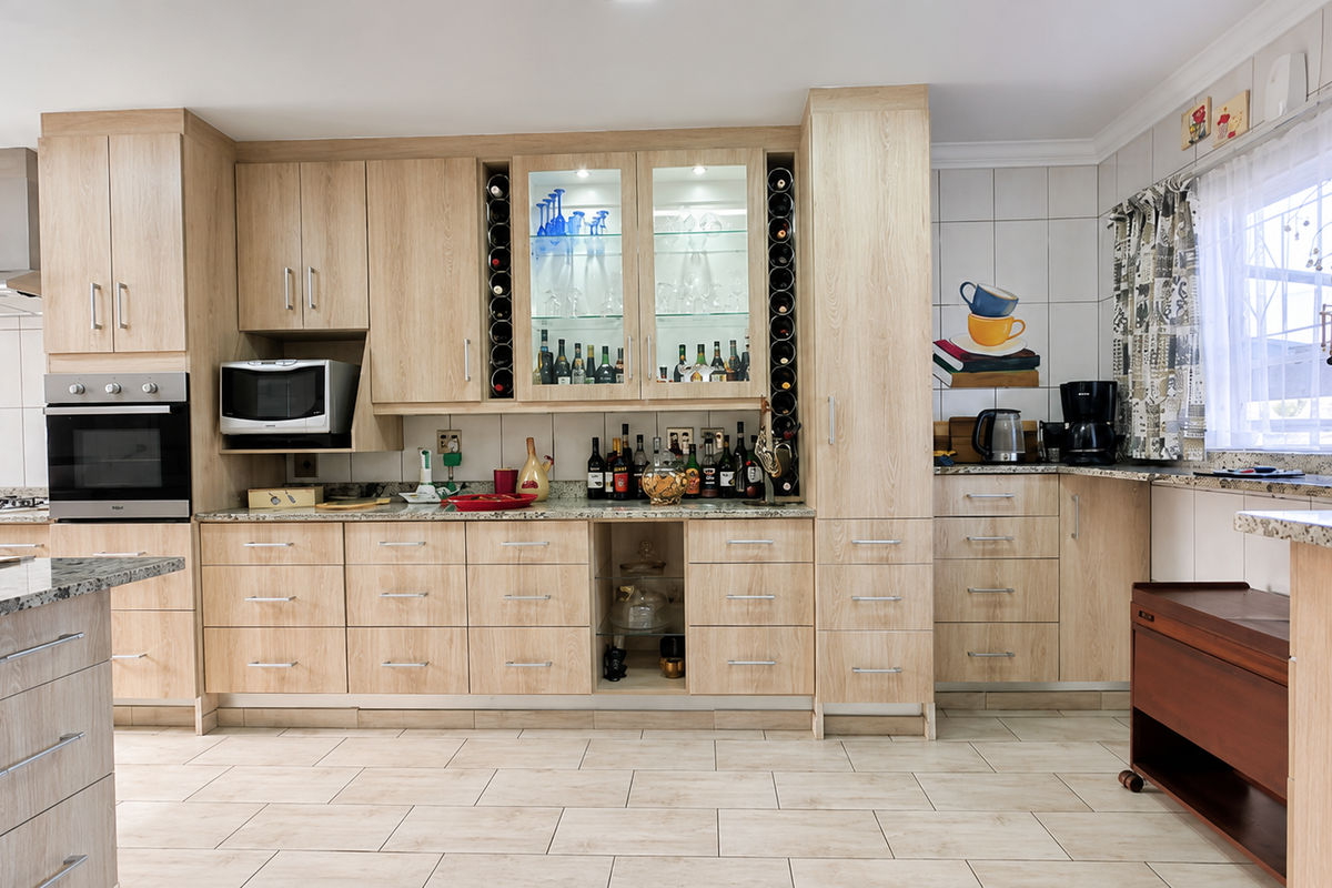 A well-maintained kitchen featuring light wood cabinetry, granite countertops, built-in oven, extractor fan, and integrated wine storage with glass-fronted display units.