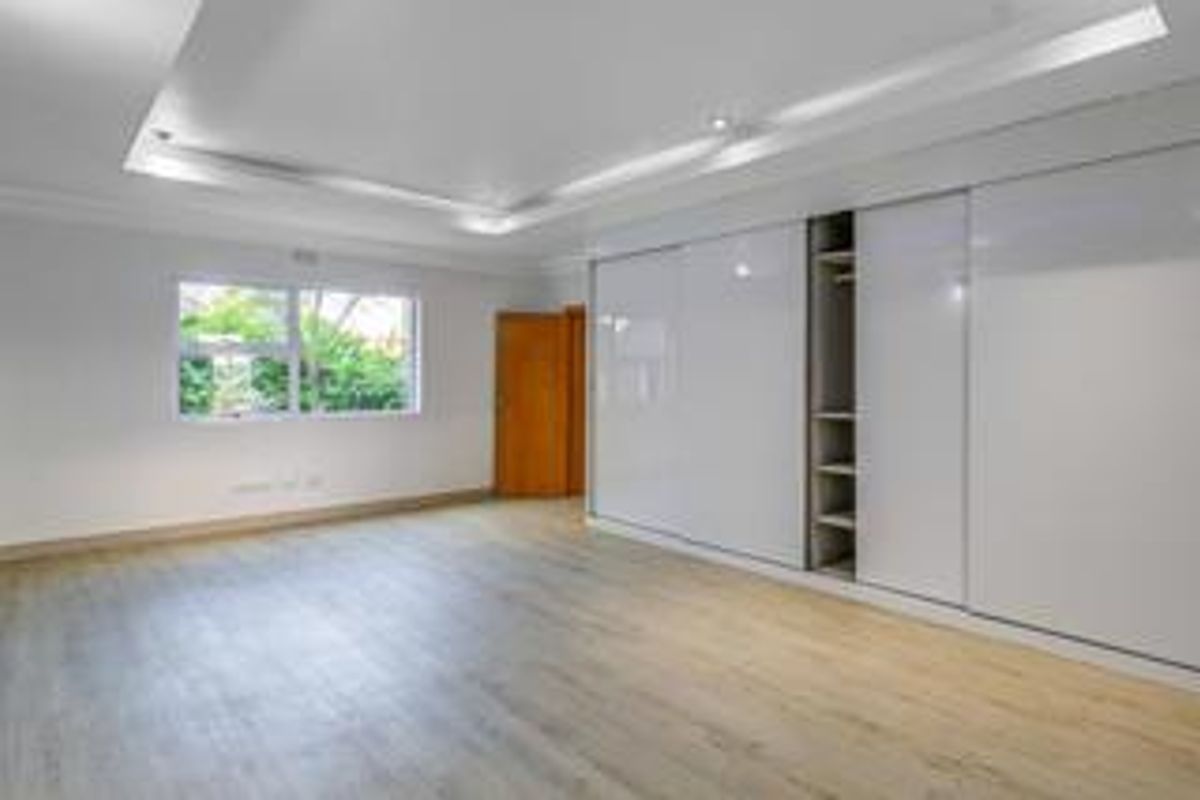 A bright, spacious bedroom featuring modern laminate flooring, recessed ceiling lighting, and a large, sleek built-in sliding door wardrobe.