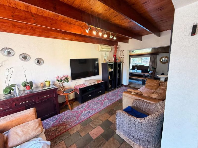 Open-plan living area featuring exposed timber ceiling beams, stone tile flooring, and a wall-mounted air conditioning unit, flowing into an adjacent dining space.
