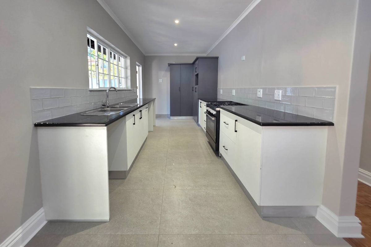 Modern galley-style kitchen featuring white cabinetry, dark countertops, subway tile backsplash, and built-in oven with gas hob.