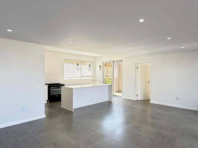 Spacious open-plan living and kitchen area featuring modern tiled floors, a central kitchen island, gas stove, and recessed lighting with direct access to the patio.