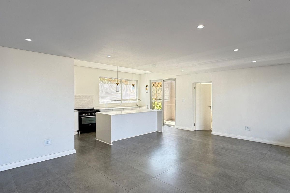 Spacious open-plan living and kitchen area featuring modern tiled floors, a central kitchen island, gas stove, and recessed lighting with direct access to the patio.