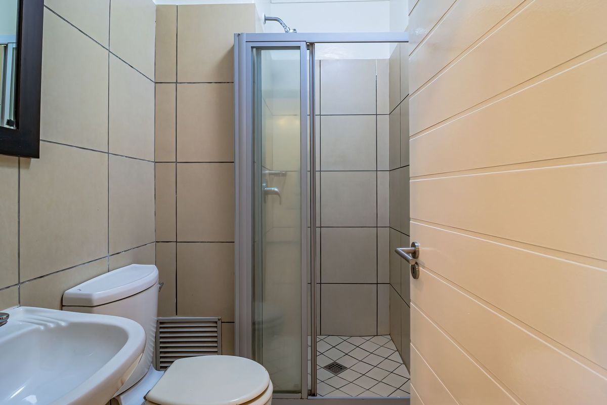A functional bathroom featuring a shower enclosure, toilet, and washbasin with neutral wall and floor tiling.