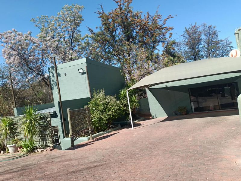 Front exterior view of the property featuring a paved driveway, covered parking area with a shade sail, and mature garden landscaping.