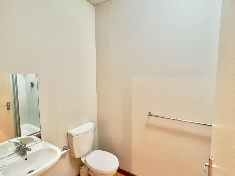 A compact guest bathroom featuring a pedestal basin, standard toilet, laminate flooring, and a drop ceiling.
