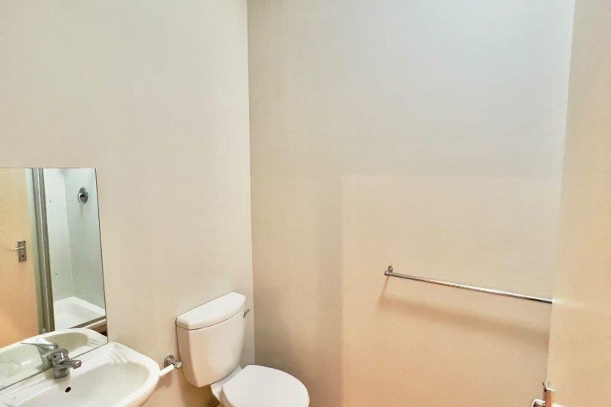 A compact guest bathroom featuring a pedestal basin, standard toilet, laminate flooring, and a drop ceiling.