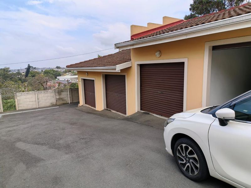 Exterior view of a triple garage unit with roller shutter doors, featuring an asphalt driveway and precast boundary walling.