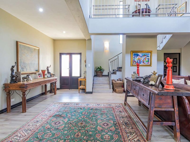 Spacious double-volume entrance hall featuring a grand staircase with metal balustrades, recessed lighting, and light-toned laminate flooring.