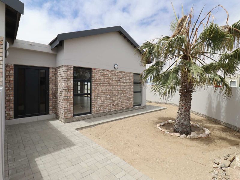 A well-maintained rear exterior view featuring a paved patio area, brick facade, and secure boundary wall.