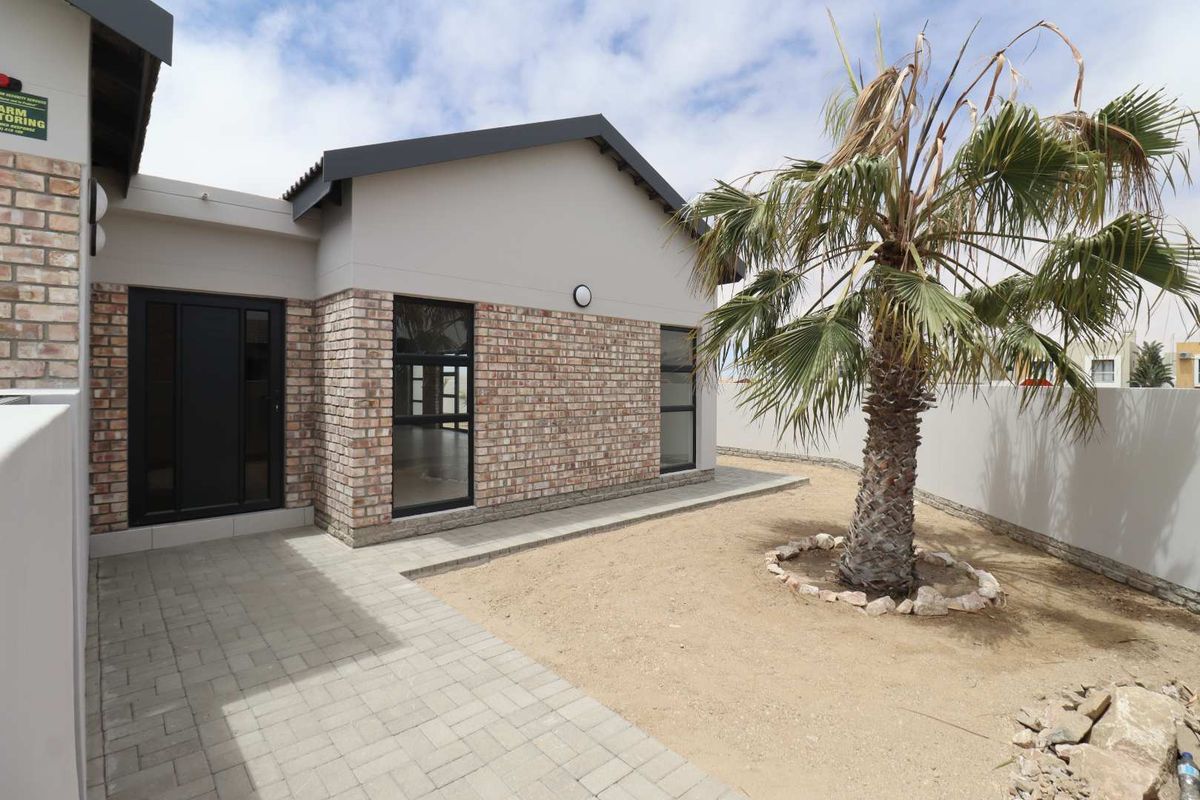 A well-maintained rear exterior view featuring a paved patio area, brick facade, and secure boundary wall.