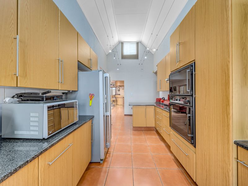 A galley-style kitchen featuring light wood cabinetry, granite countertops, a double wall oven, and a high vaulted ceiling with recessed lighting.