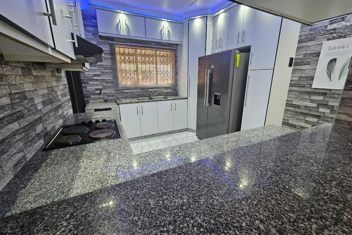 Modern kitchen featuring granite countertops, white cabinetry, electric hob, extractor fan, and tiled splashback with integrated lighting.