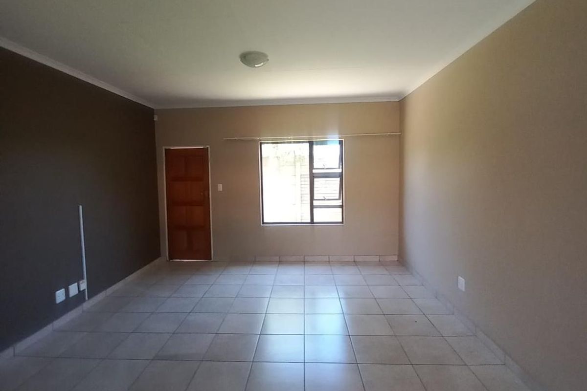 A spacious, empty living area featuring neutral wall tones, tiled flooring, and natural light from a central window.