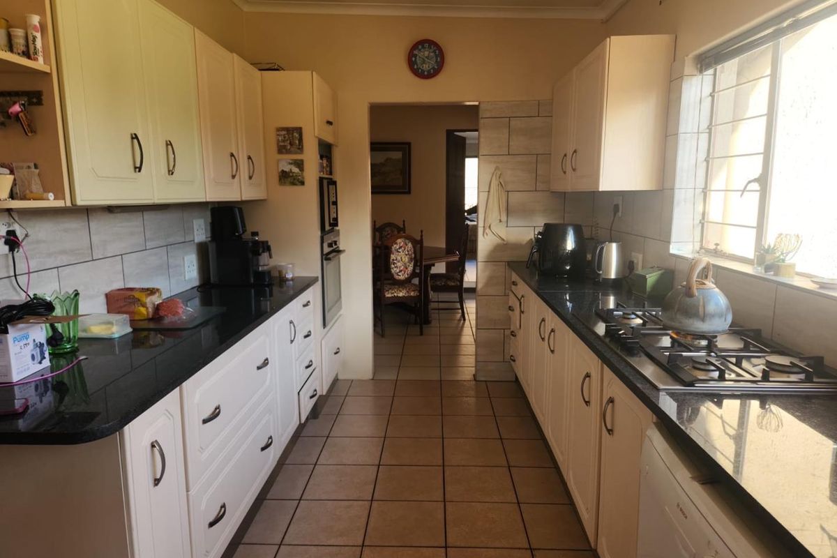 A functional galley-style kitchen featuring granite countertops, built-in cabinetry, a gas hob, and an integrated oven with tiled flooring throughout.