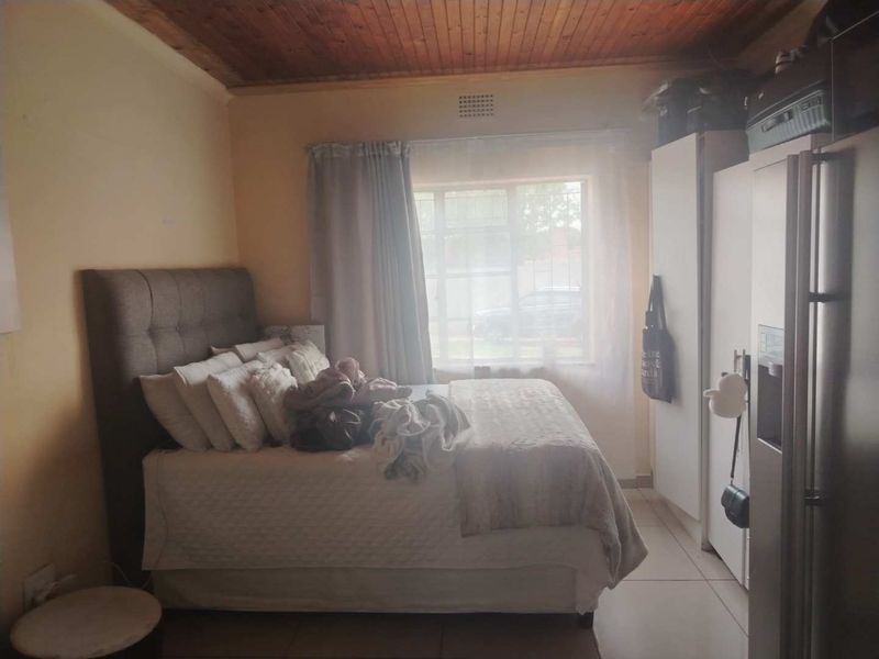 A bedroom featuring a timber ceiling, tiled flooring, and built-in cupboards, providing a functional space with natural light.