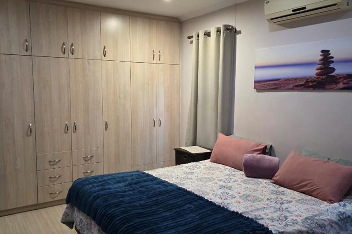 A well-maintained bedroom featuring extensive built-in wooden cabinetry, recessed ceiling lighting, and a wall-mounted air conditioning unit.
