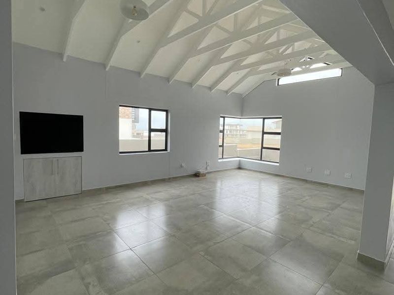 Spacious living area featuring a high vaulted ceiling with exposed trusses, large windows for natural light, and modern tiled flooring.