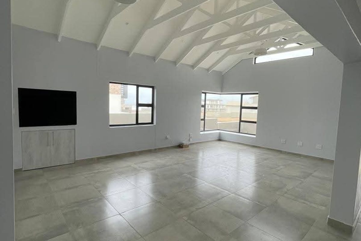 Spacious living area featuring a high vaulted ceiling with exposed trusses, large windows for natural light, and modern tiled flooring.