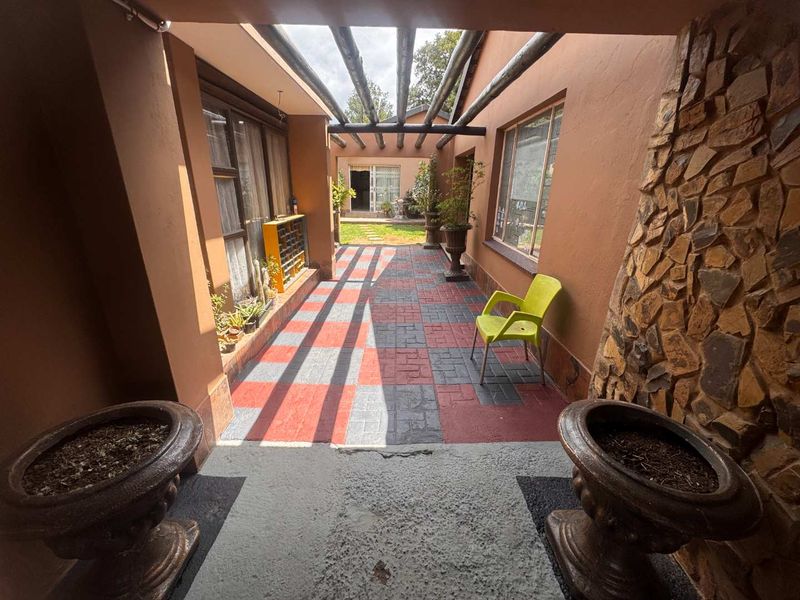 Covered patio area featuring exposed timber beams, stone cladding, and paved flooring, providing a transition space between the interior and the rear garden.