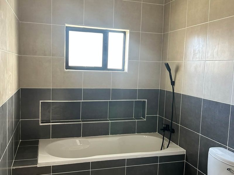 A modern bathroom featuring a built-in bathtub with a recessed wall niche, tiled walls, and a standard toilet.