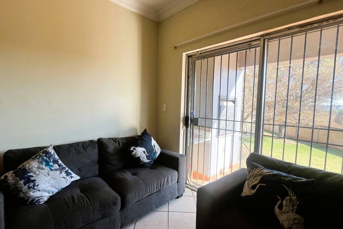 A living room featuring tiled flooring and a sliding glass door with an integrated security gate, providing access to the outdoor area.