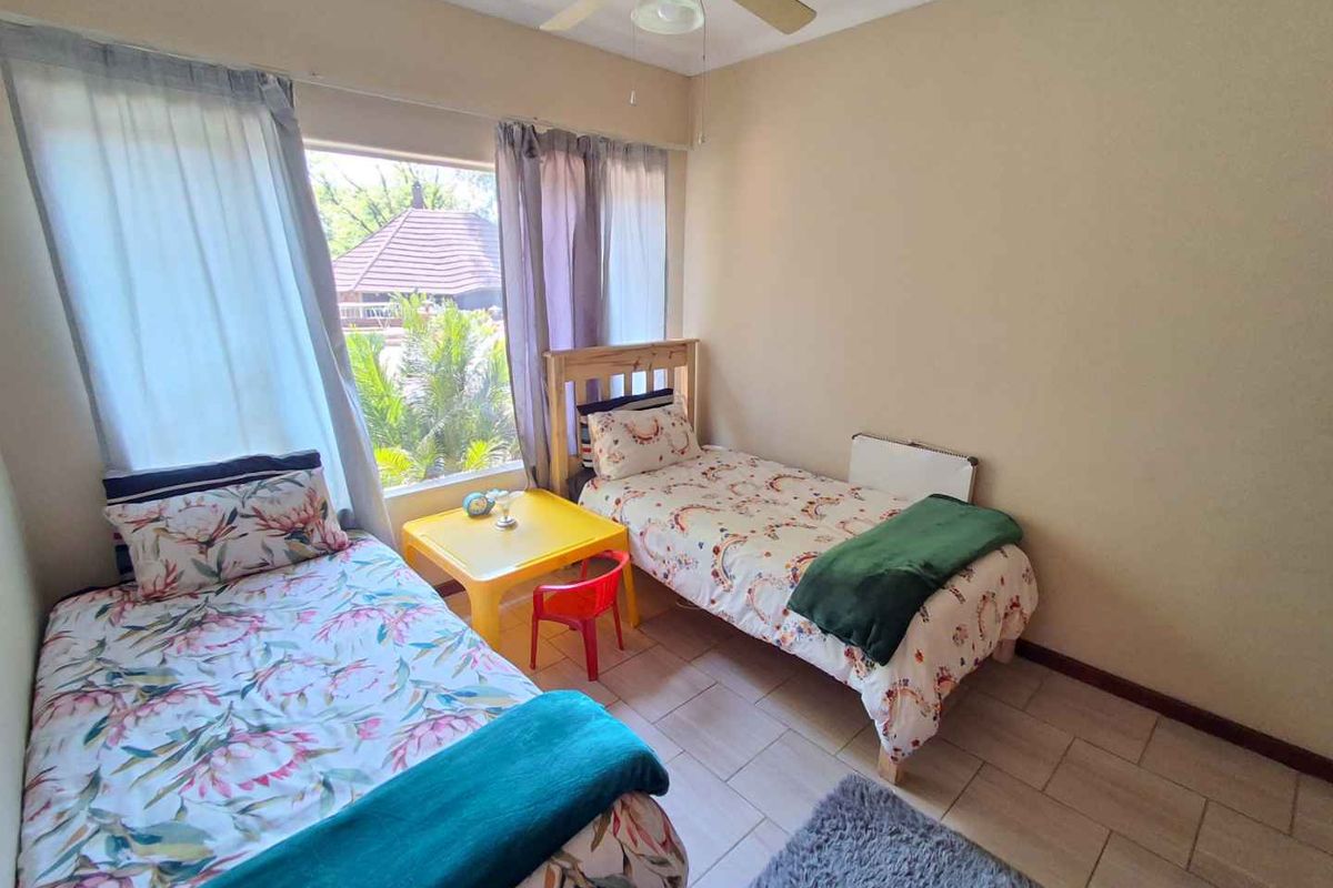A functional bedroom featuring tiled flooring, a ceiling fan, and a large window providing natural light.