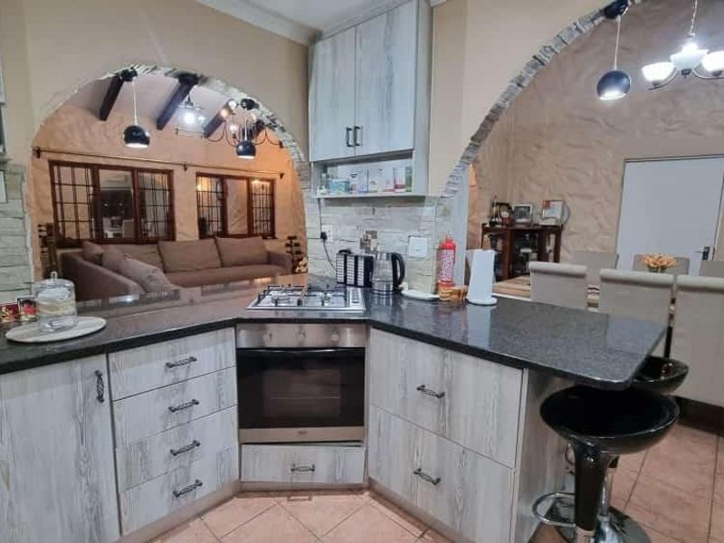 Open-plan kitchen featuring granite countertops, built-in oven and gas hob, flowing into the dining and living areas through distinctive brick archways.