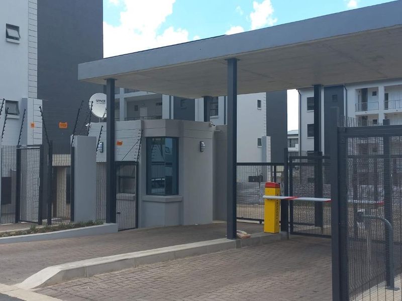 Secure apartment complex entrance featuring a guard house, boom gate access control, and perimeter electric fencing.
